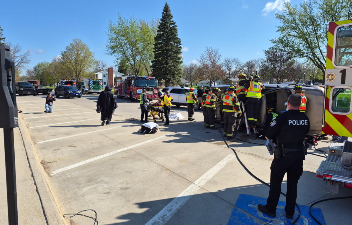 Emergency responders and a police officer surround an overturned vehicle during a rescue at a parking lot.