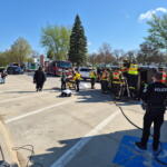 Emergency responders and a police officer surround an overturned vehicle during a rescue at a parking lot.