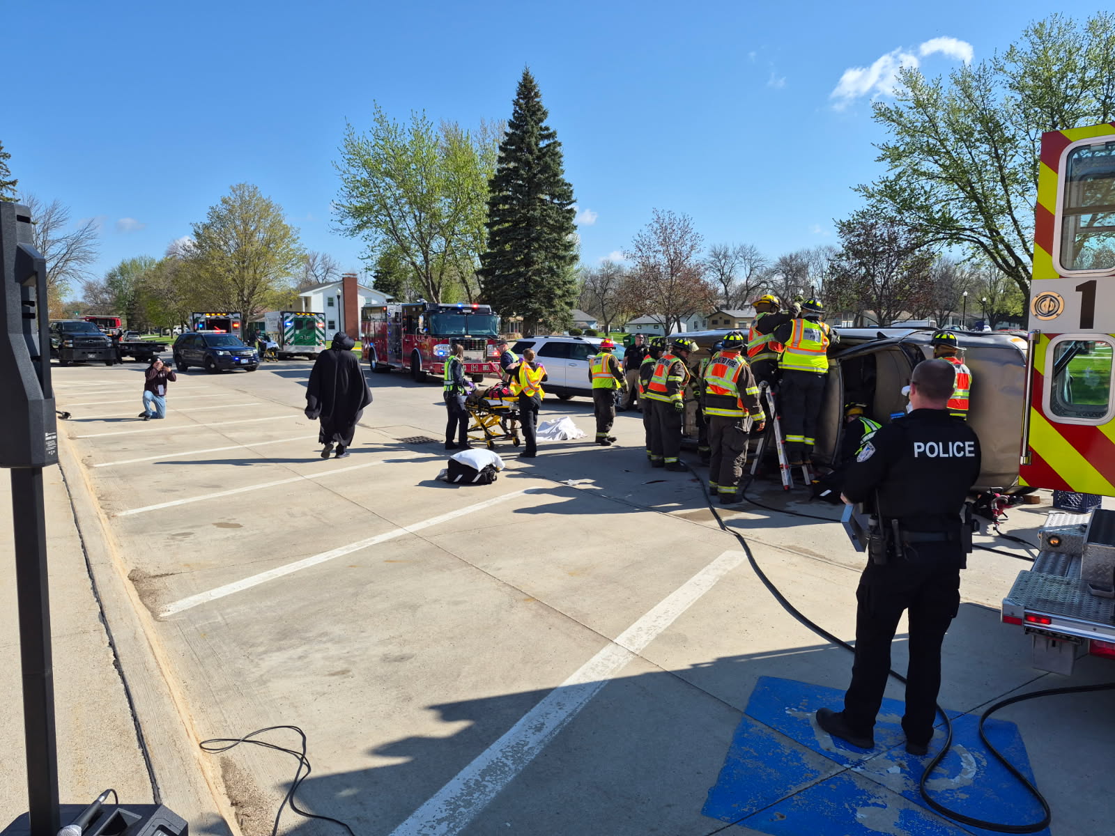 Emergency responders and a police officer surround an overturned vehicle during a rescue at a parking lot.