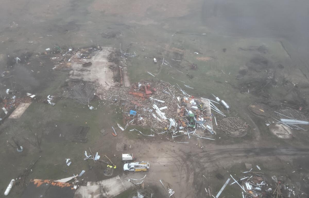 Aerial view of a property ruined by destruction, with scattered debris and collapsed structures across a muddy yard.