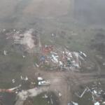 Aerial view of a property ruined by destruction, with scattered debris and collapsed structures across a muddy yard.