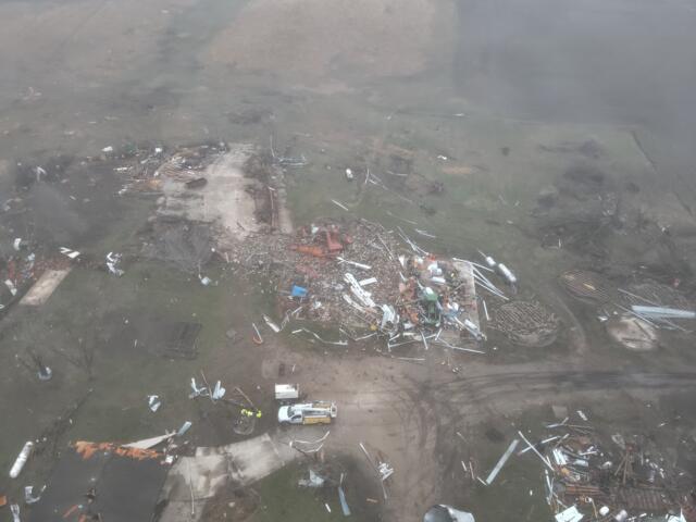 Aerial view of a property ruined by destruction, with scattered debris and collapsed structures across a muddy yard.