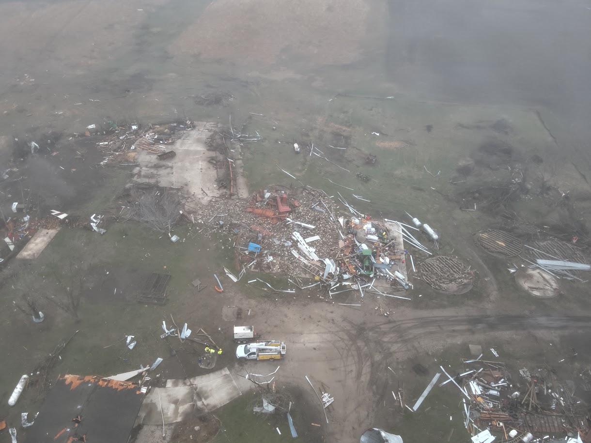 Aerial view of a property ruined by destruction, with scattered debris and collapsed structures across a muddy yard.
