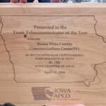 Wooden plaque engraved with Iowa outline, awarded to Buena Vista County Communications Center/911 as Team Telecommunicator of the Year, dated April 20, 2026, with Iowa APCO seal and slogan.