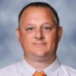 Head-and-shoulders portrait of a man in a white shirt and orange tie, with a blue-gray backdrop.