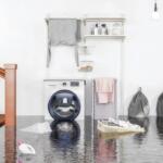 Laundry room flooded with water on the floor; a front-loading washer sits beside a drying rack and ironing board visible in the background.