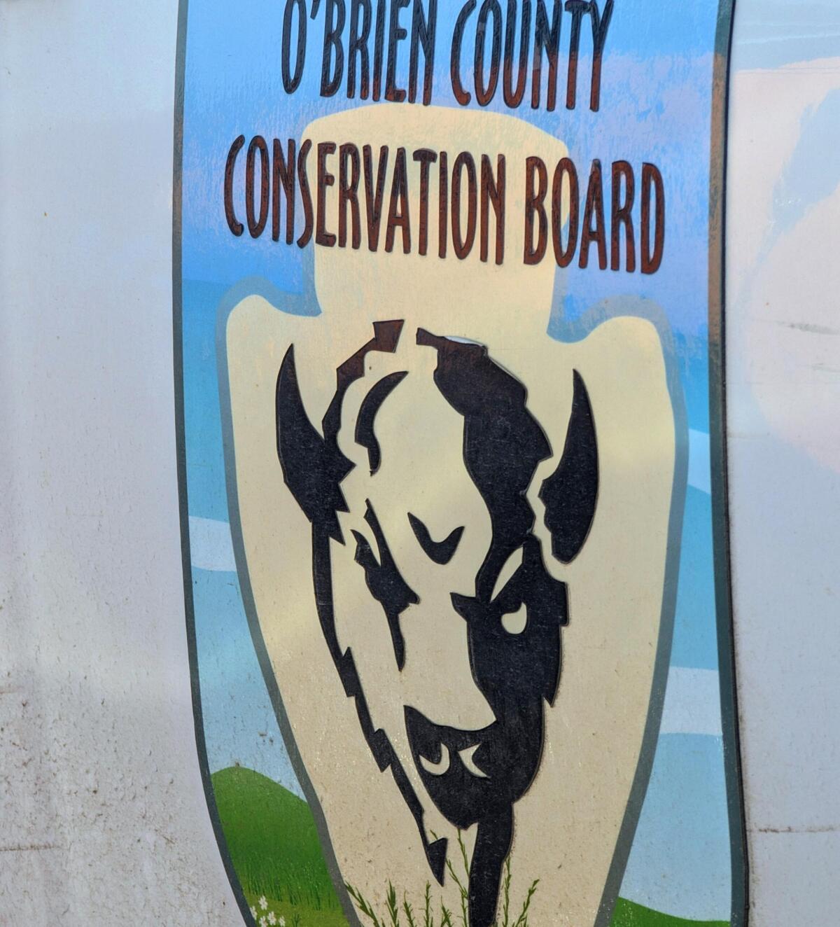 Sign for O'Brien County Conservation Board with a beige shield and two black bison silhouettes on a blue background.