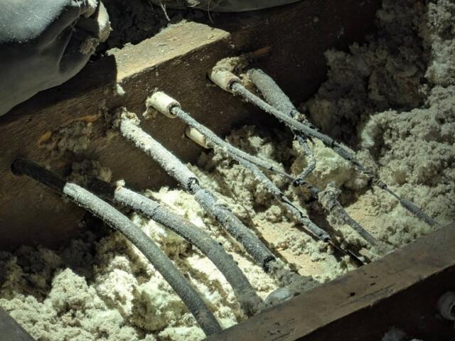 Close-up of frost-covered electrical cables embedded in a wooden trench, surrounded by snow or ice.