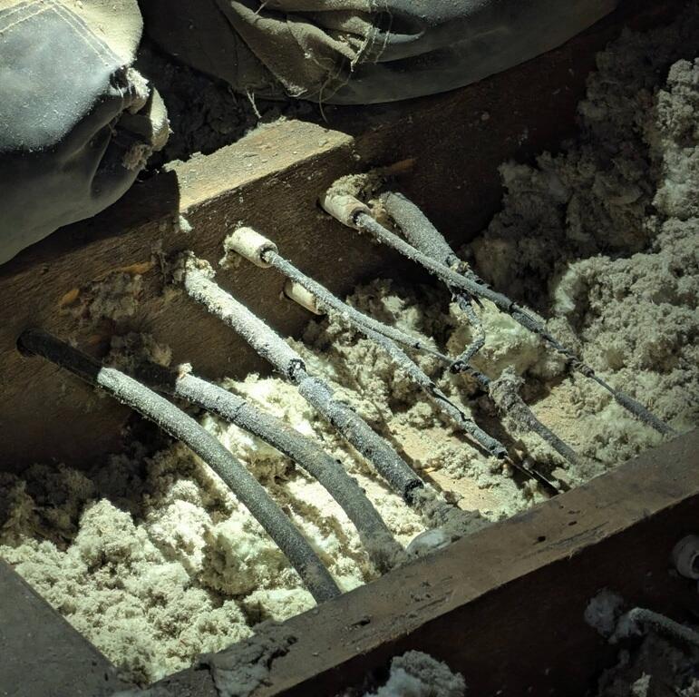 Close-up of frost-covered electrical cables embedded in a wooden trench, surrounded by snow or ice.