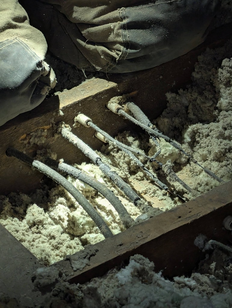 Close-up of frost-covered electrical cables embedded in a wooden trench, surrounded by snow or ice.