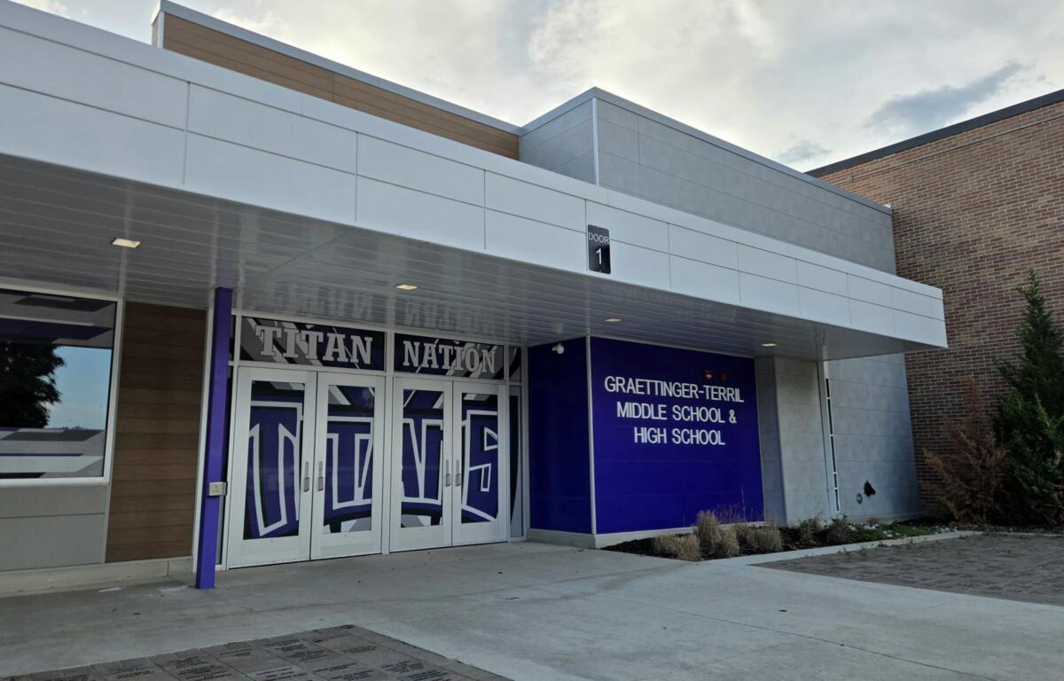 Front entrance of a modern school building with decorative glass doors featuring a large 'Titan Nation' graphic and a blue wall with the Graettinger–Terril Middle School & High School sign to the right.