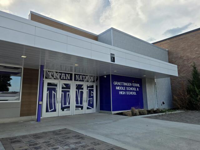 Front entrance of a modern school building with decorative glass doors featuring a large 'Titan Nation' graphic and a blue wall with the Graettinger–Terril Middle School & High School sign to the right.