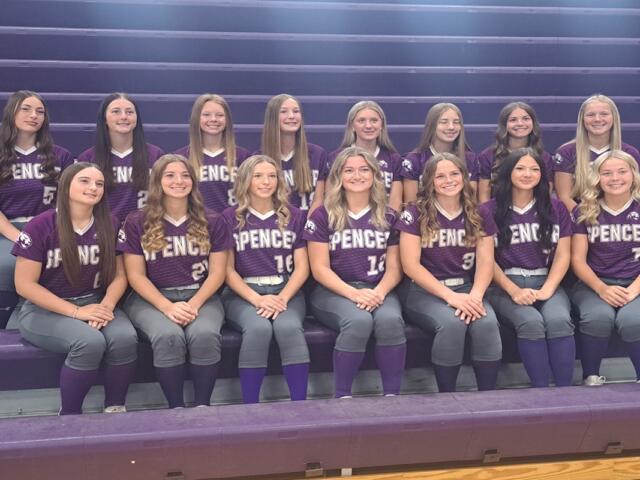 Group of girls in purple Spencer softball jerseys posing on gym bleachers.